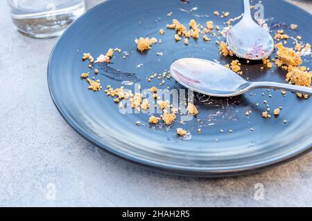 Empty dark plate with crumbs and dirty spoon on a table after sweet pie. Stock Photo