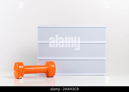 Fitness dumbbells with empty lightbox on white table. Mockup concept. Stock Photo
