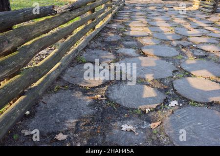Near a wooden fence made of logs, there is a wooden pavement made of many round wooden stumps dug into the ground of various shapes. Stock Photo