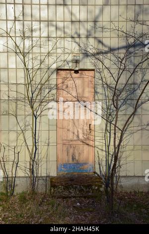 An old closed door in a wall covered with rectangular tiles. The shadows of tree branches without leaves are reflected on the wall Stock Photo