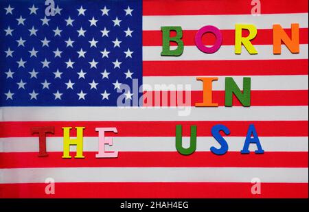 On the US flag, the text BORN IN THE USA is lined with multicolored decorative letters. Stock Photo