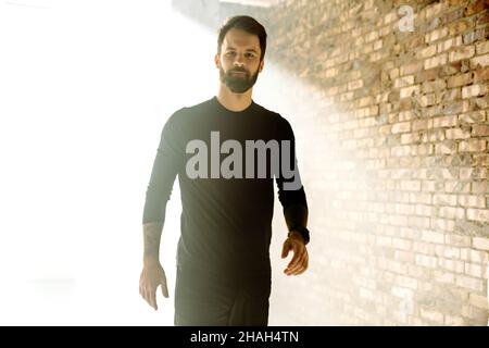 Mid aged bearded sportsman wearing smartwatch standing indoors Stock Photo
