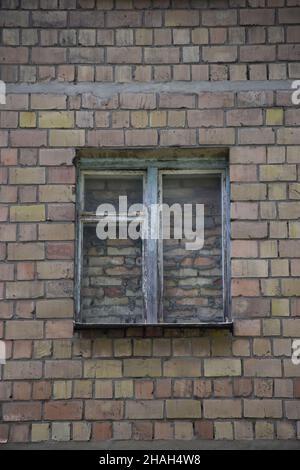 In the center of the brick wall there is an old window completely covered with brickwork, walled up with bricks and cement Stock Photo