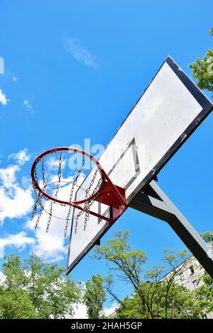 Basketball hoop and backboard against a bright blue sky with white clouds and trees. Shot from below Stock Photo