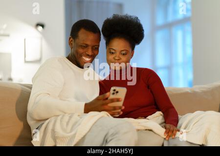 Smiling young african couple at home making videocall on smartphone, chatting online Stock Photo