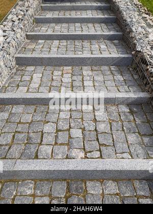 Sidewalk steps of tiled stone lined with rows, leaving in perspective with borders decorated with boulders Stock Photo