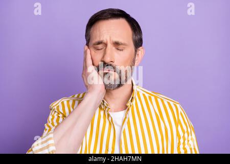 Photo of unhappy upset mature man dressed yellow shirt arm cheek having toothache isolated purple color background Stock Photo