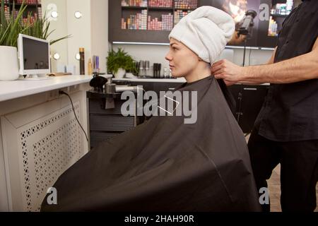 Hairdresser putting hairdressing cape on client in beauty salon Stock Photo