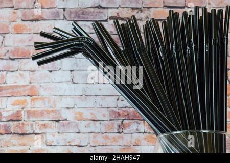 Several dozen decorative black cocktail tubes in a glass against the background of a brick wall. On the left there is a place for an inscription Stock Photo