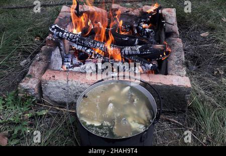 Fish soup cooked over a fire, cooked in a large saucepan next to a grill lined with bricks lit on the ground Stock Photo