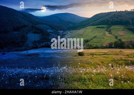 day and night time change concept above mountainous countryside landscape. pastures and rural fields near the forest on the hills. beautiful early aut Stock Photo