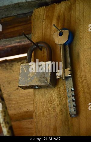 There is a bunch of different keys and a padlock on the wooden wall. Stock Photo