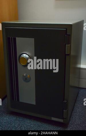 A small locked safe with a code and a lock is on the floor on the carpet Stock Photo