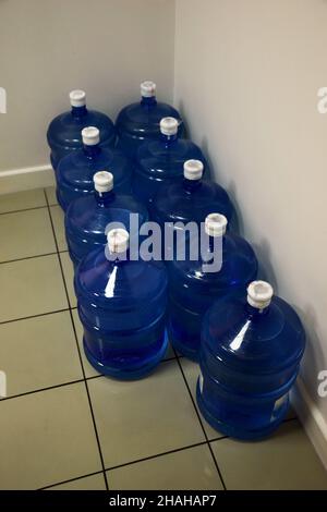 About ten large plastic bottles of filtered clean water in rows in the corner of the room Stock Photo