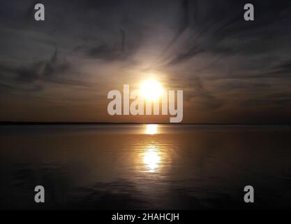 Sea surface of water without waves at sunset with not a bright sun above the horizon Stock Photo