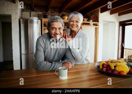 Portrait of happily retired elderly biracial couple leaning on kitchen counter, smiling at camera. Healthy lifestyle in modern kitchen. Stock Photo