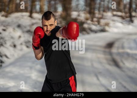 Strong boxer with boxing gloves standing in nature at snowy winter day and sparring. Boxing in nature, healthy life, winter sport Stock Photo