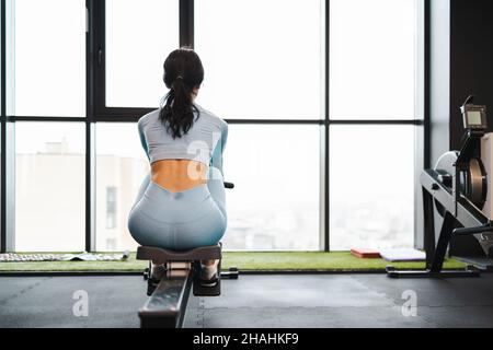 Back view of a woman using a rowing machine in the gym Stock Photo