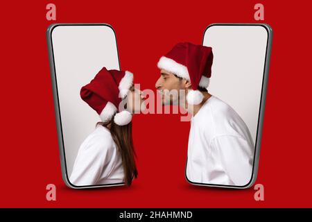 Dating App. Couple In Santa Hats Peeking Out Of Smartphones And Kissing Stock Photo