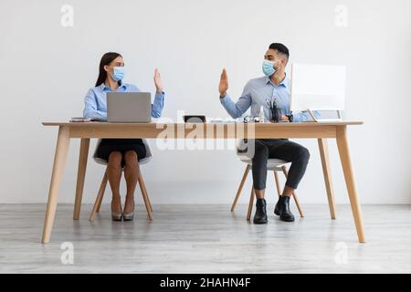 Colleagues in disposable face masks greeting each other waving hands Stock Photo