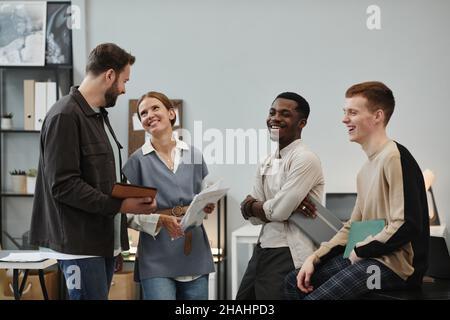 Group of young colleagues laughing and talking to each other while standing at office after meeting Stock Photo
