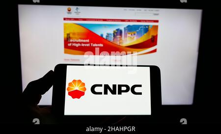 Person holding smartphone with logo of company China National Petroleum Corporation (CNPC) on screen in front of website. Focus on phone display. Stock Photo