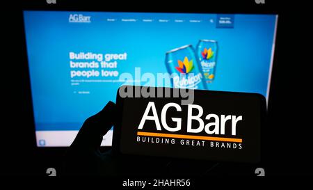 Person holding smartphone with logo of British soft drink company A.G. Barr plc on screen in front of website. Focus on phone display. Stock Photo