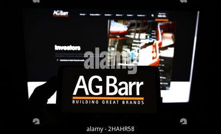 Person holding mobile phone with logo of British soft drink company A.G. Barr plc on screen in front of business webpage. Focus on phone display. Stock Photo