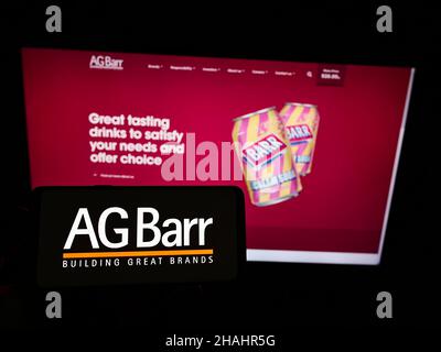 Person holding cellphone with logo of British soft drink company A.G. Barr plc on screen in front of business webpage. Focus on phone display. Stock Photo