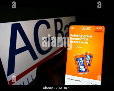 Person holding cellphone with webpage of British soft drink company A.G. Barr plc on screen in front of logo. Focus on center of phone display. Stock Photo