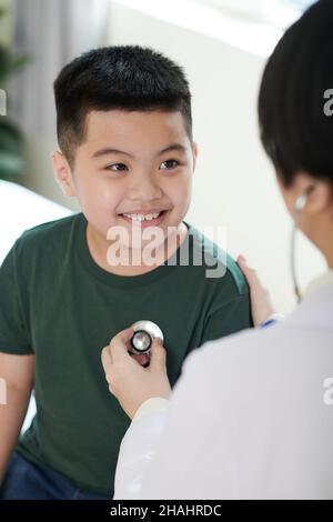 Smiling preteen boy looking at general practitioner who is checking his breath Stock Photo
