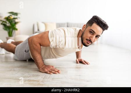 Attractive young Arab man standing in plank pose or doing push ups on mat at home Stock Photo