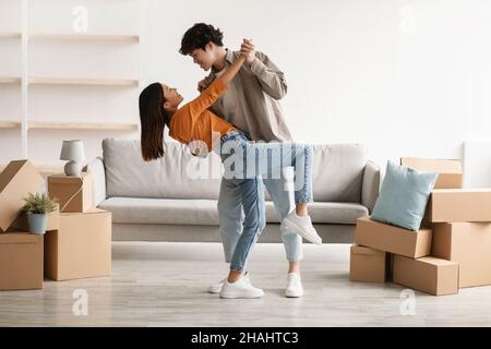 Affectionate young Asian couple dancing in their house among cardboard boxes on moving day, full length Stock Photo