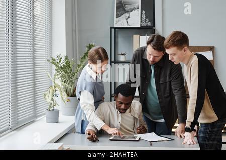 Businesswoman pointing at digital tablet and discussing with her colleagues new project during their teamwork at office Stock Photo