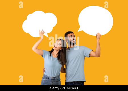 Portrait of young arab couple holding empty speech bubbles with space for your text on yellow studio background Stock Photo