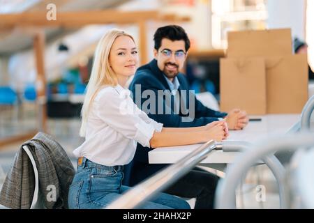 Beautiful young man and woman waiting coffee, resting sitting at table in mall after shopping at mall, looking at camera. Stock Photo