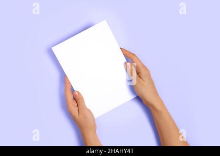 Top view of woman hands holding mockup blank paper greeting or invitation card over lilac pastel background. Color of year 2022. Christmas, Valentine Stock Photo
