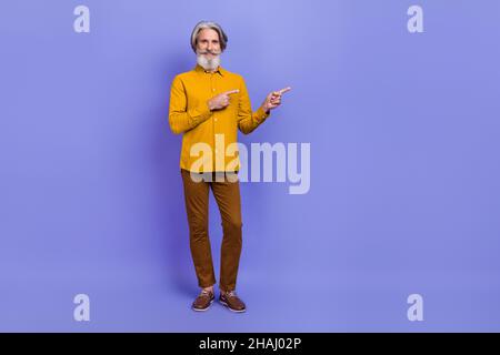 Full length body size view of attractive cheery gray-haired man showing copy space isolated over bright violet purple color background Stock Photo