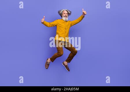 Full length body size view of attractive cheery gray-haired man jumping showing thumbup isolated over bright violet purple color background Stock Photo