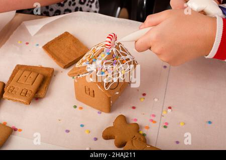 Kids assembling and decorating a gingerbread house at Christmas time. Christmas family tradition, Christmas crafts. Stock Photo