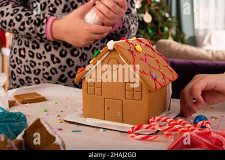 Kids assembling and decorating a gingerbread house at Christmas time. Christmas family tradition, Christmas crafts. Stock Photo