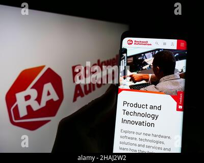 Person holding smartphone with webpage of US company Rockwell Automation Inc. on screen in front of logo. Focus on center of phone display. Stock Photo