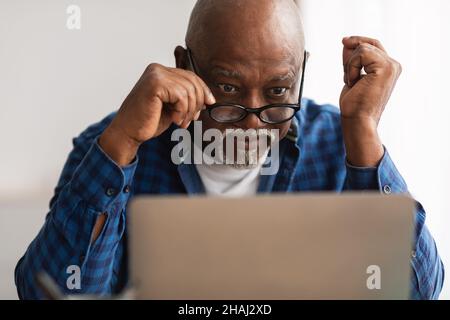 Shocked Senior African Man Looking At Laptop Above Eyeglasses Indoor Stock Photo