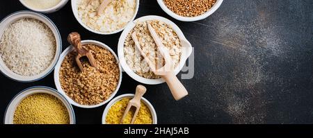 Variety of cereal flakes rice, millet, buckwheat, oatmeal. Superfood in white ceramic bowls on dark old concrete background. Top view. Stock Photo