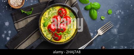 Frittata with arugula, potatoes and cherry tomatoes in iron pan on old stone table background. Top view. Stock Photo