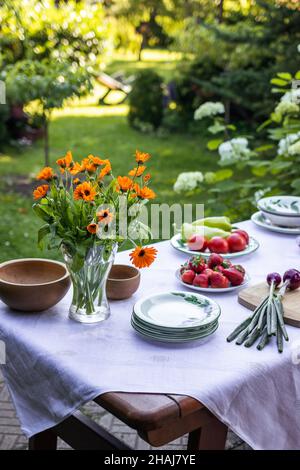 Dining table ready for garden party. Place setting with plates, vegetable, fruits and bouquet marigold flowers Stock Photo
