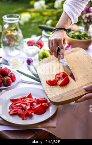 Chopped tomatoes on cutting board. Woman cooking fresh vegetable salad in garden Stock Photo