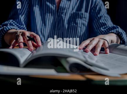 Minsk, Belarus - October 30 2021 Student hands closeup holding pen and reading many books. Concept of research and searching answers in textbooks and academic literature. Stock Photo