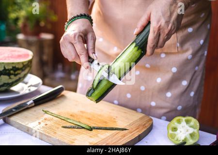 Woman peeling cucumber. Making fresh vegetable salad outdoors. Preparing raw food Stock Photo