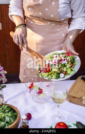 Woman making fresh vegetable salad. Mixing chopped food in glass salad bowl Stock Photo
